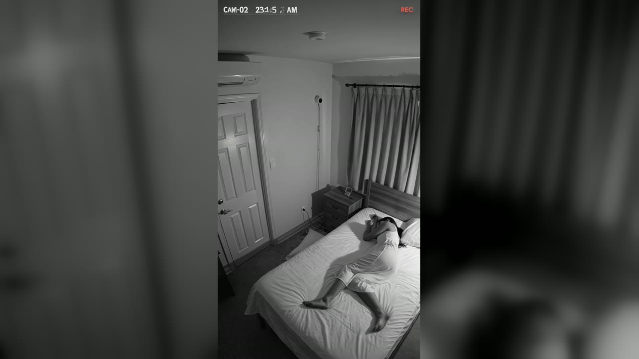 Still frame from Sleeping Woman Slides Toward the Headboard, Then the Curtain Swells With the Window Shut